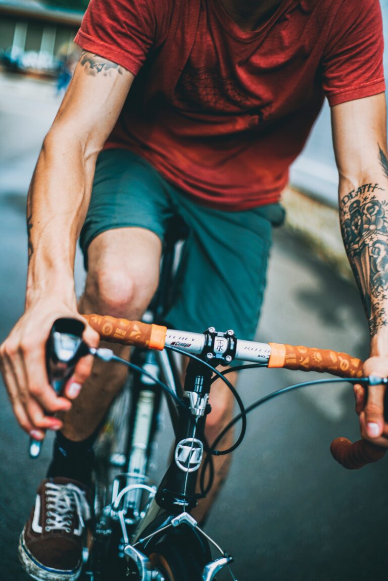 Dynamische Nahaufnahme eines Radfahrers in Fahrt, der den Lenker mit braun-orange gemustertem Griffband fest im Griff hat, mit Fokus auf die muskulösen Arme.