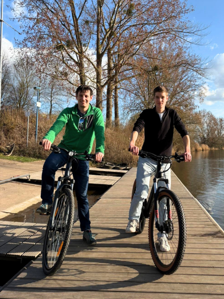 Zwei junge Männer auf Mountainbikes, die auf einem Steg stehen.