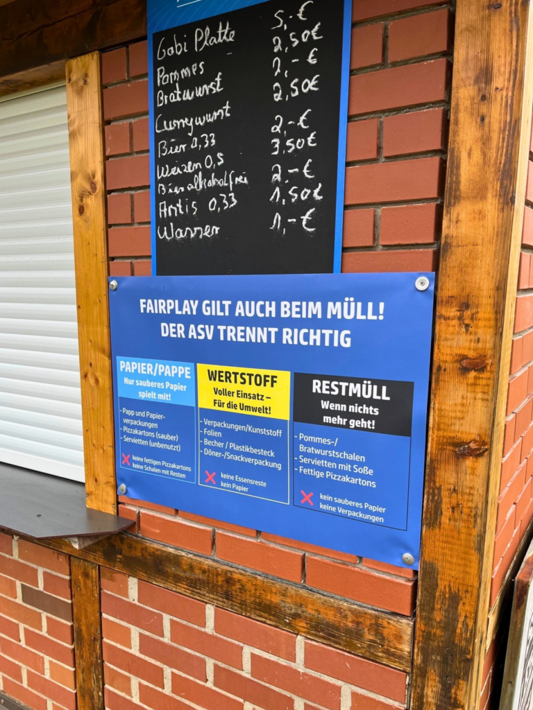 Schild an einer Wand mit Essensgerichten und darunter hängt ein Schild zur korrekten Mülltrennung.