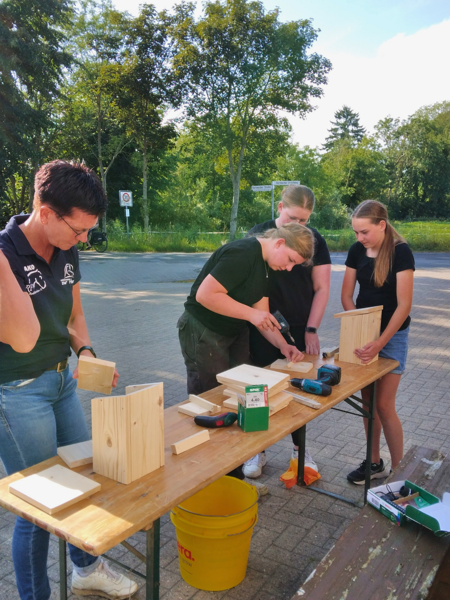 Vier Personen an einem Tisch, die mit Holz Vogelhäuser bauen.