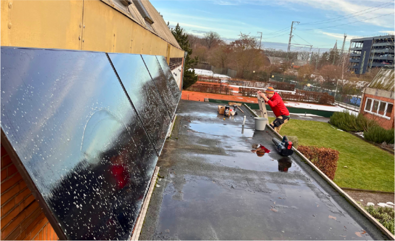 Eine Person klettert eine Leiter rauf auf ein Flachdach. An der Wand daneben sind vier Solarpanele befestigt.