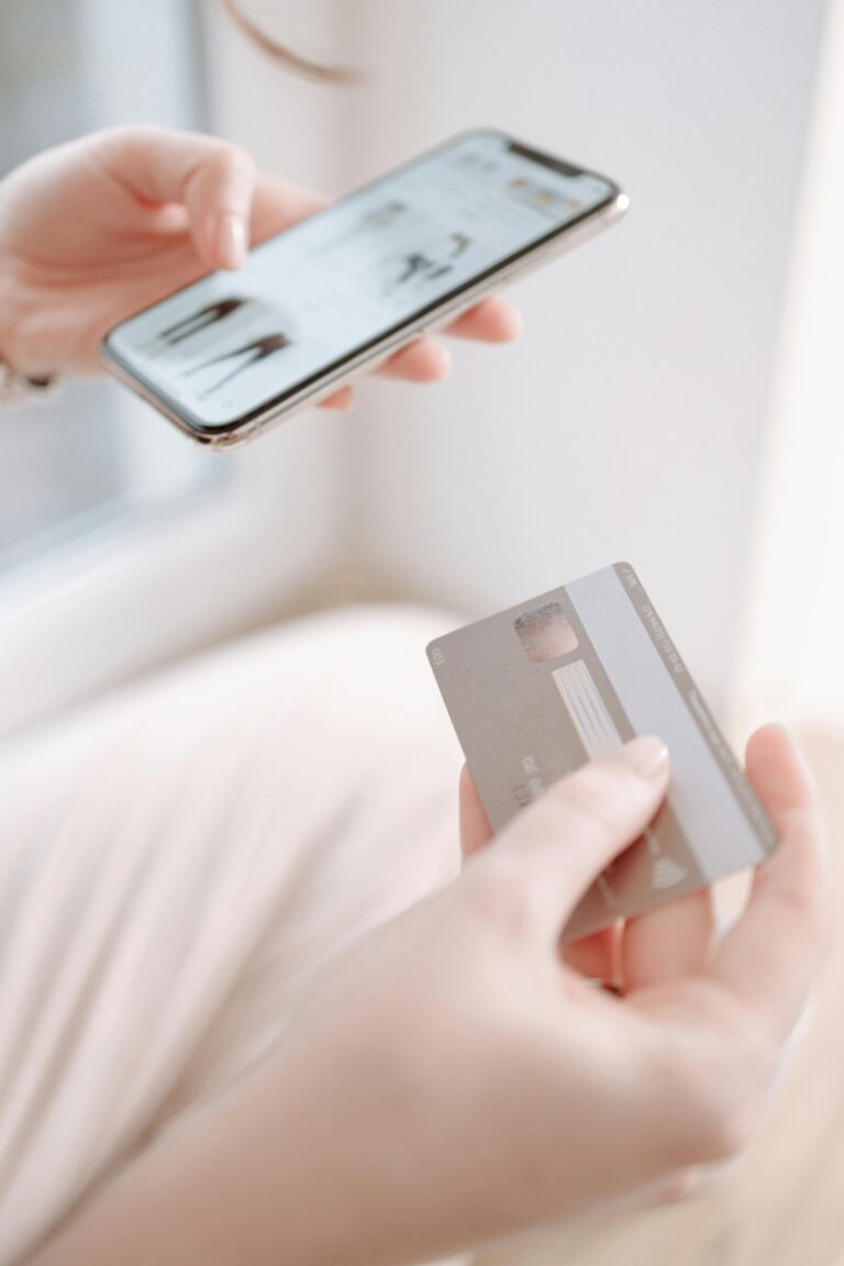 Nahaufnahme von Händen, die ein Smartphone und daneben eine Kreditkarte halten.