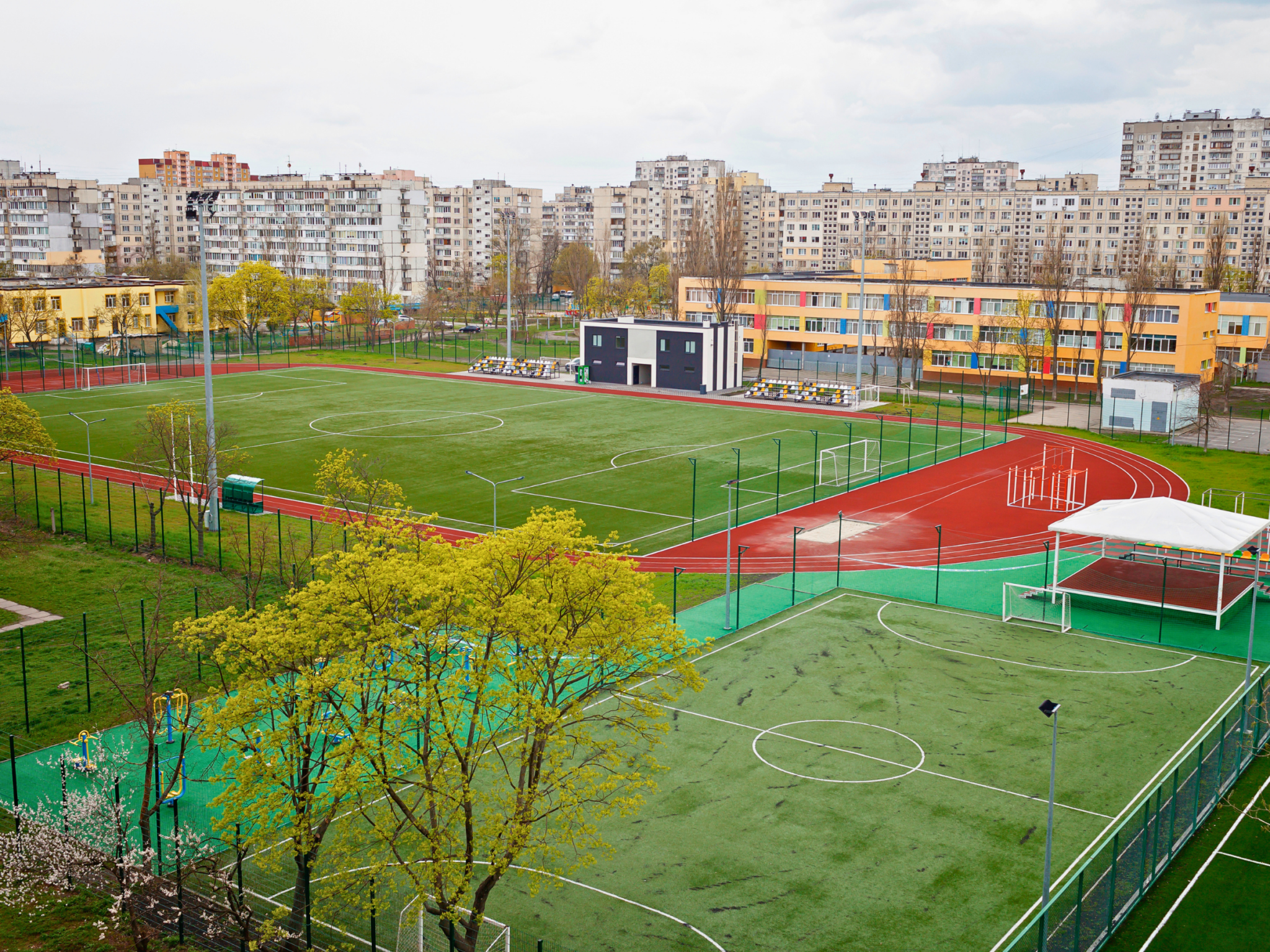 Eine moderne Außensportanlage mit Fußballfeldern und einer Laufbahn vor einer Kulisse aus Wohnblöcken.