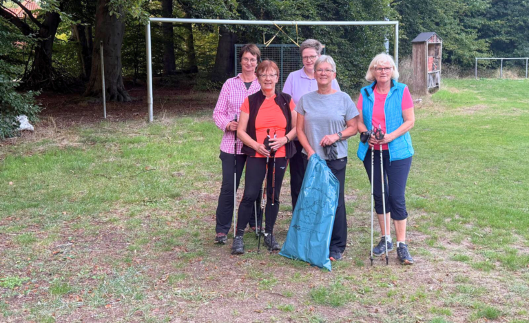 Fünf Frauen beim Plogging im Rahmen einer Aktion des KreisSportBund Diepholz. Sie stehen sportlich gekleidet auf einem Rasenplatz, halten Nordic-Walking-Stöcke und einen großen, blauen Müllsack.