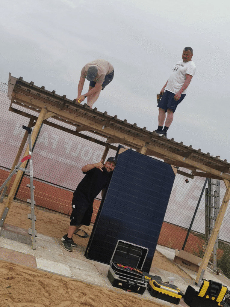 Drei Männer bauen eine Balkon-Solaranlage auf einem Unterstand auf.